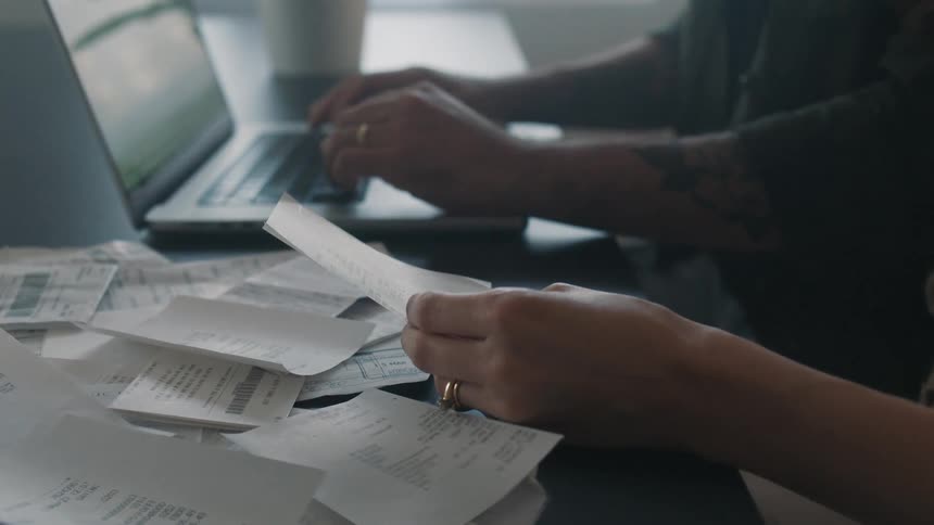 Coworkers sit and deal with receipts while one of them types on laptop