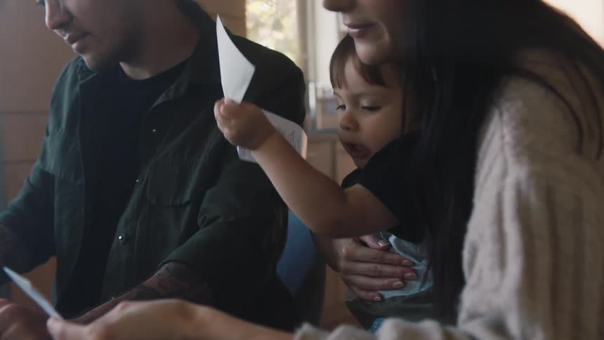 A woman is holding her young son on her lap as she looks at a piece of paper and he takes it out of her hands and there is a man sitting on the couch next to them