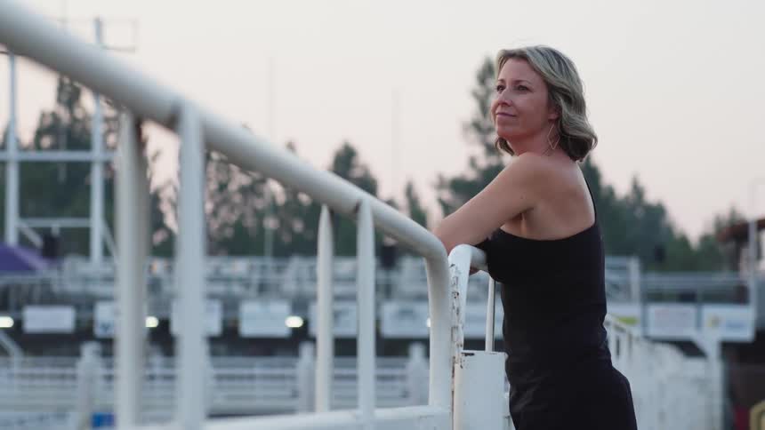 A woman smiling as she leans into the metal railing of a corral