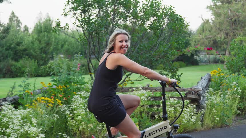 Woman pedals an electric bicycle along a country road lined with flowers