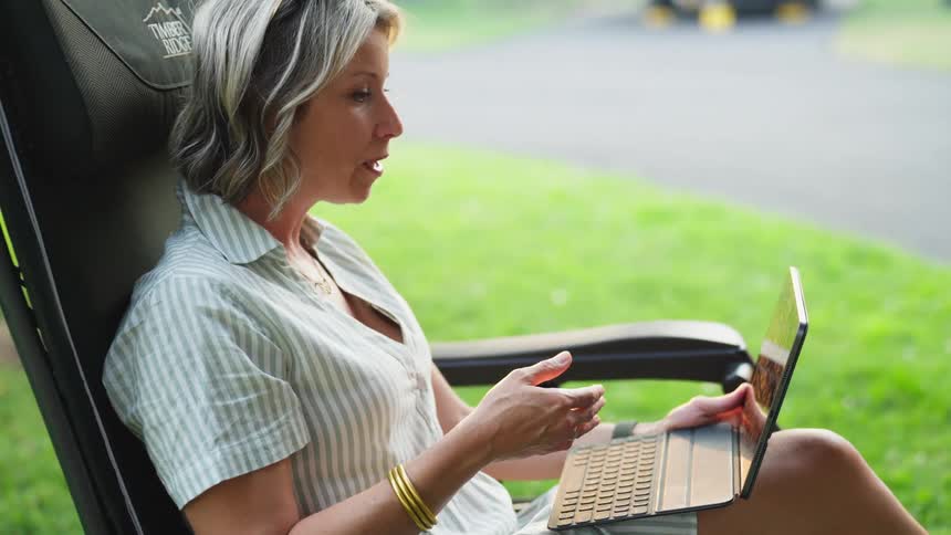 A woman sits on a chair and talks through a laptop in a suburb