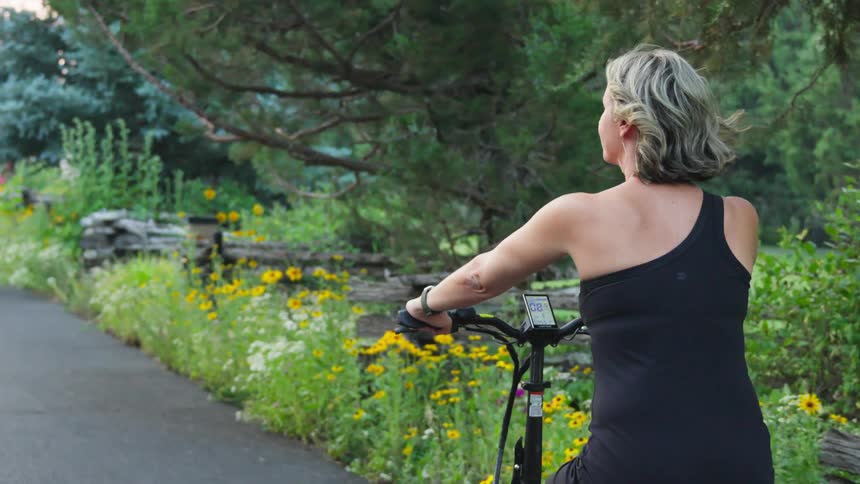 A white woman rides a bicycle on a path through a garden