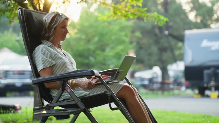A woman sits back in the chair while using her laptop outside