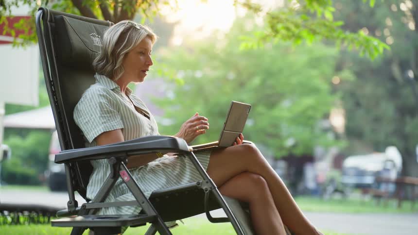 Woman sitting in the backyard of a house talking on an ipad
