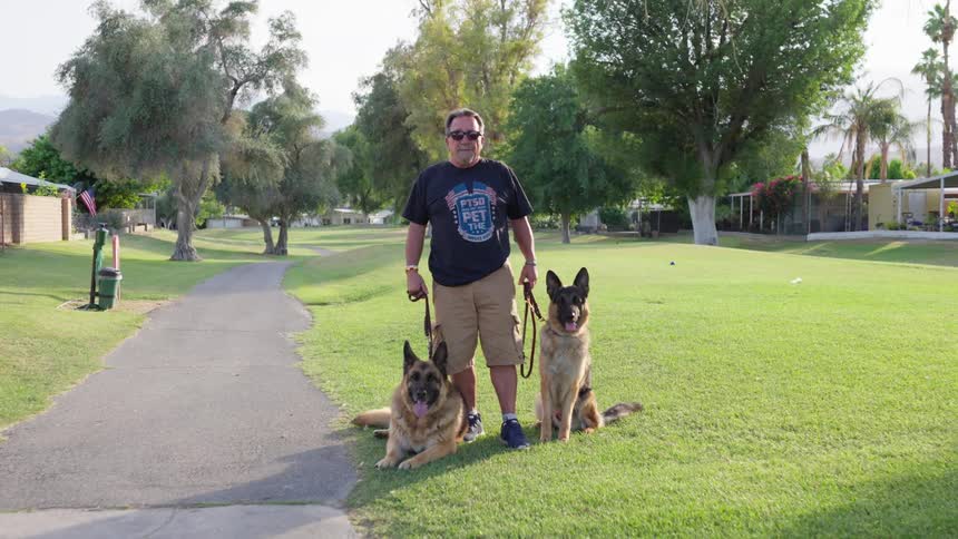 Man standing in an open air environment with two dogs by his side