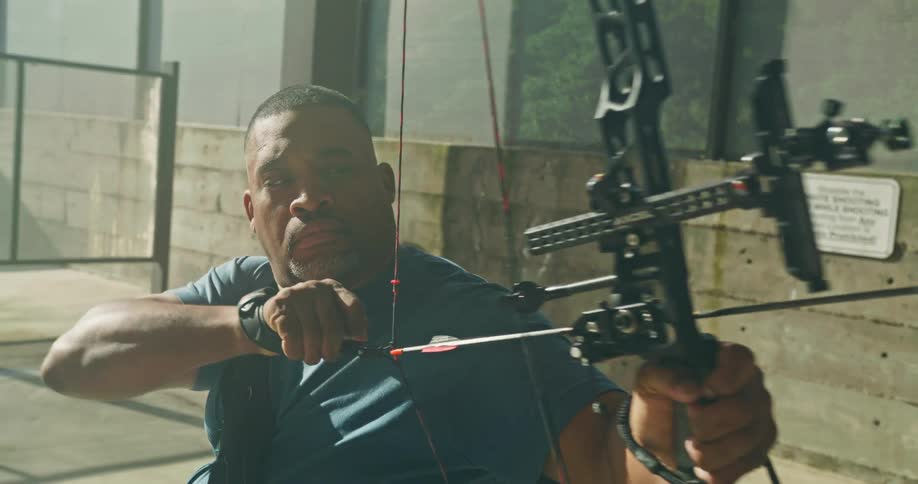 A man using a professional string bow to aim an arrow then letting the string relax instead of shooting