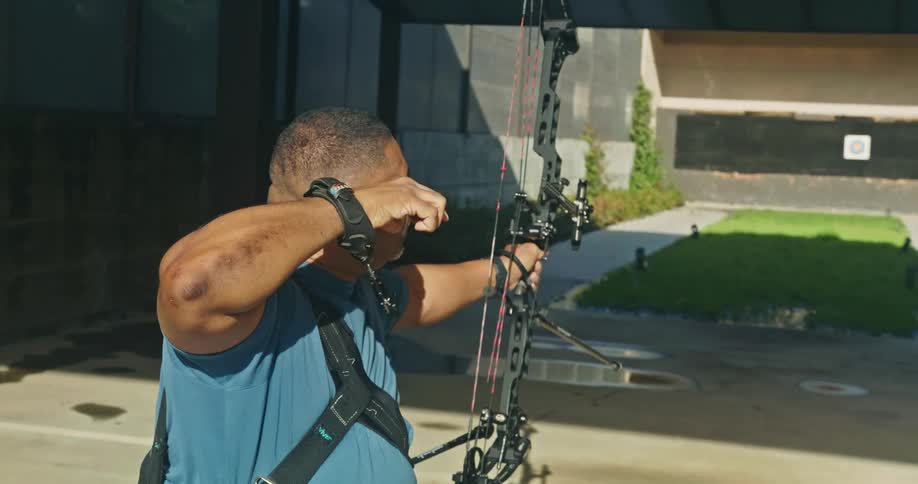 An archer draws a compound bow aiming at a target outdoors