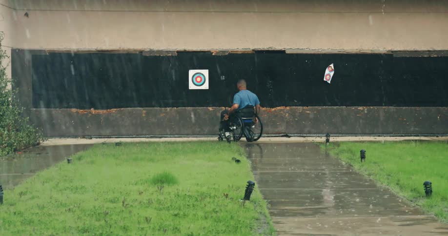 Man maneuvers his wheelchair along a sidewalk towards a target during a rainstorm