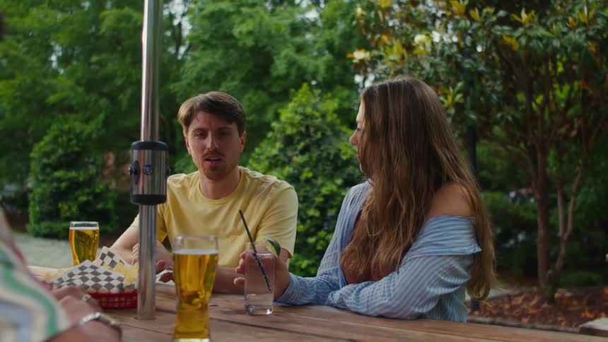 Friends sitting outdoors at a picnic table with food hold a conversation