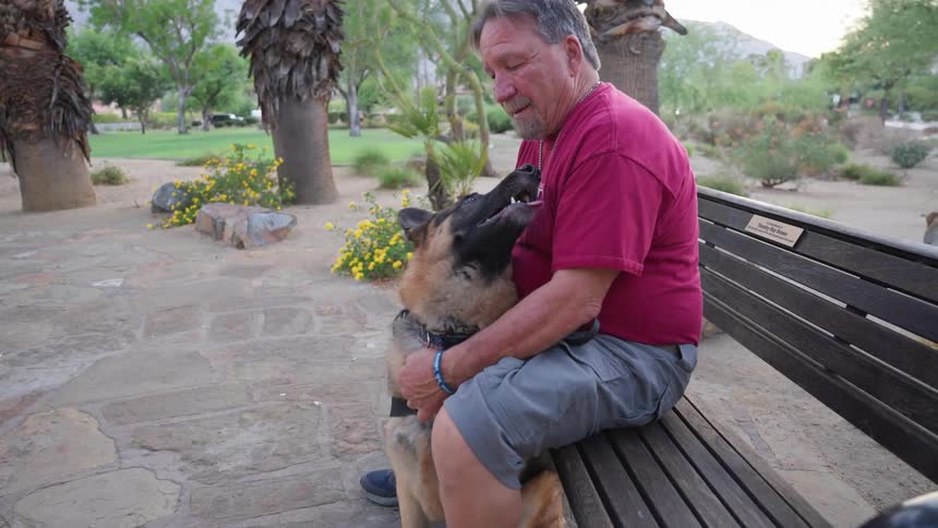 Man sitting on a bench in a square with his dog licking his feet