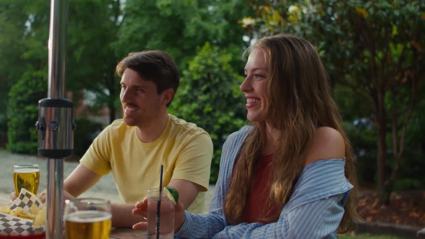 A man and a woman have fun sitting with friends and having food and drinks outdoors