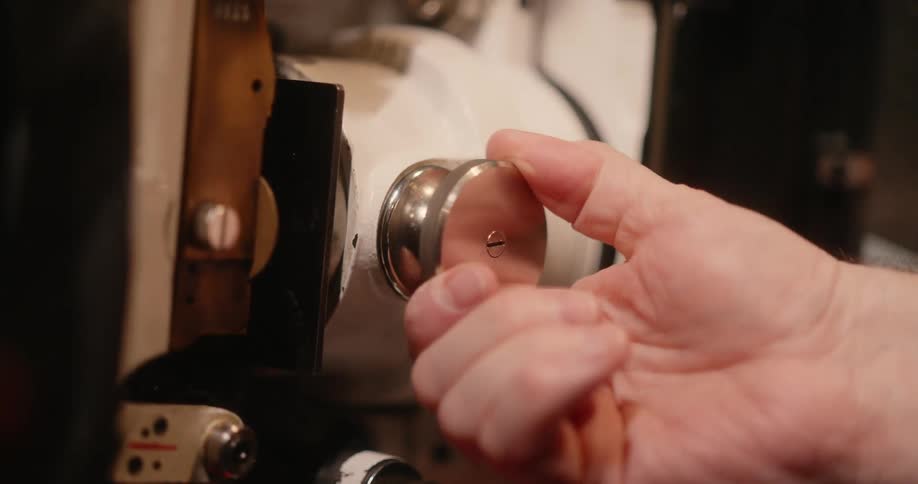 A hand turns a metal knob in a machine making a square part in the machine move back and forth as the knob is turned