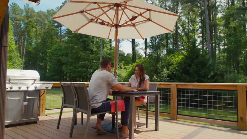 A man and a woman sit at a table on a large wooden deck