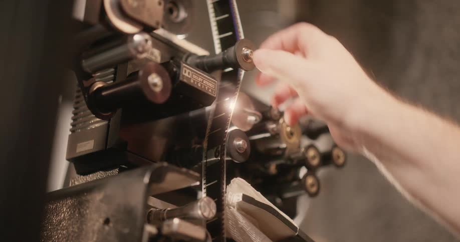 Closeup of a film projector with reels and mechanical parts visible and a hand operating it