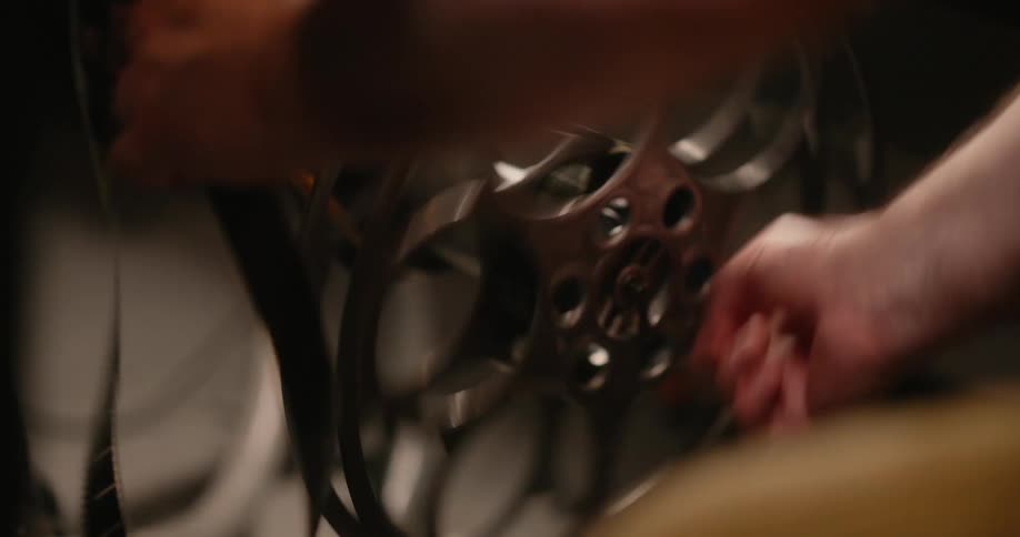 Pair of hands of a man turning an old cinema instrument and inserting a film strip