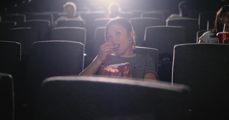 Woman sitting in a movie theater eats popcorn while watching the movie
