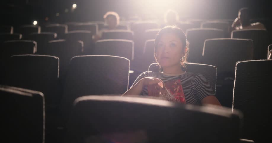 Woman eating popcorn while watching a movie at the theater laughs