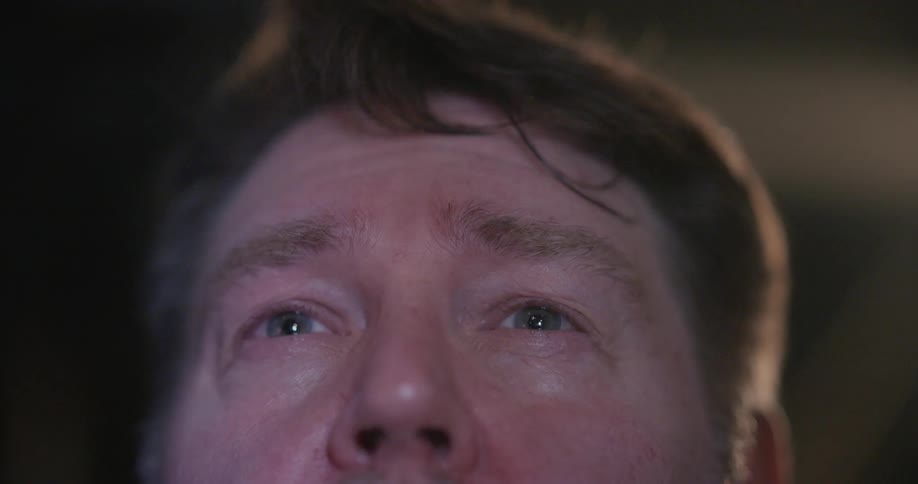 Light from the movie screen illuminates the face of a man sitting in the cinema