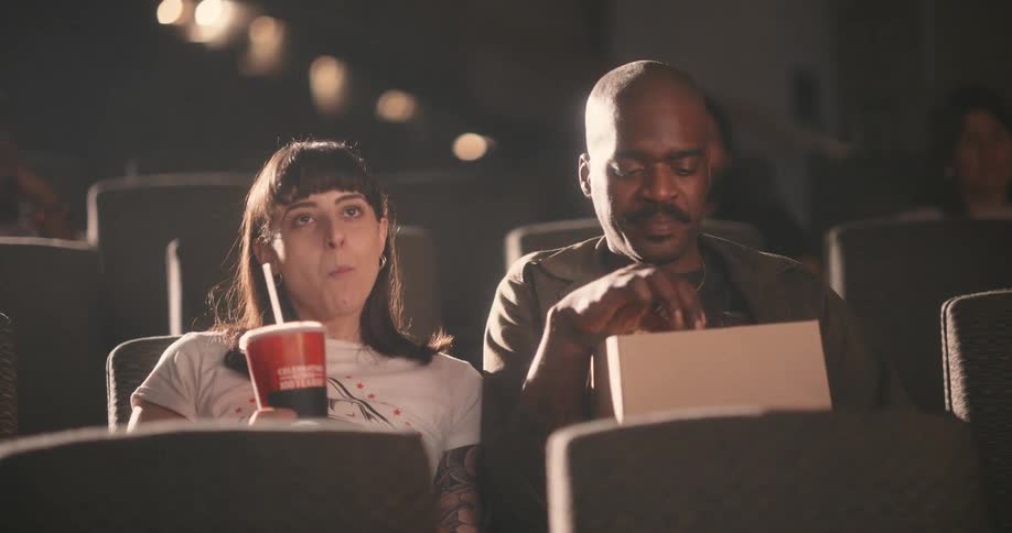 Friends share popcorn while watching a movie in a movie theater