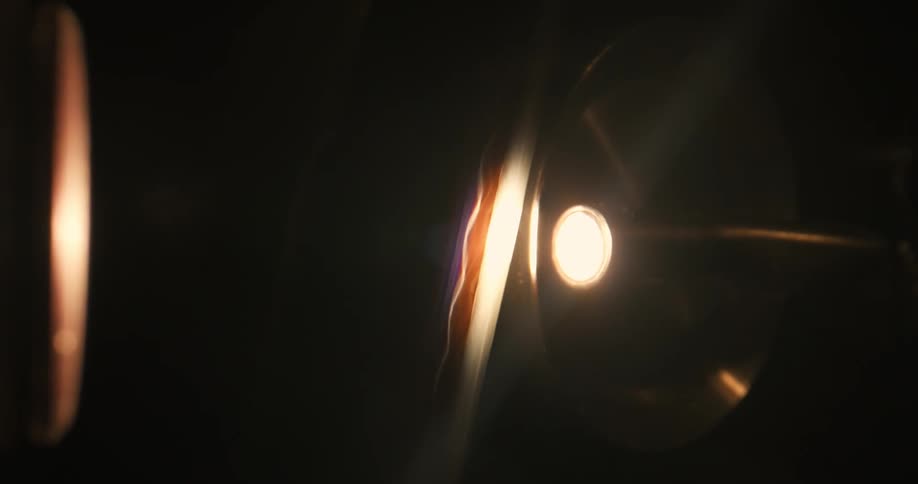 A closeup of a strip of vintage film rolling in front of the bright light of a projector