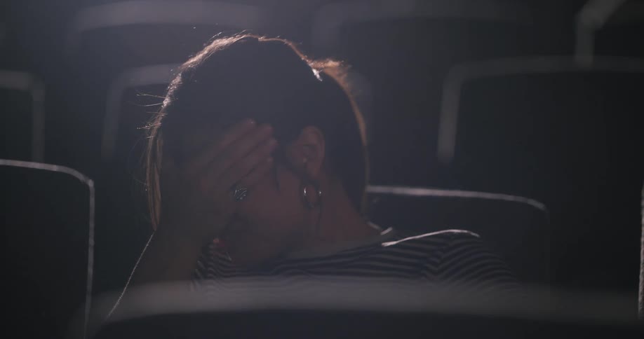 Woman putting her hand on her face while sitting in a movie theater
