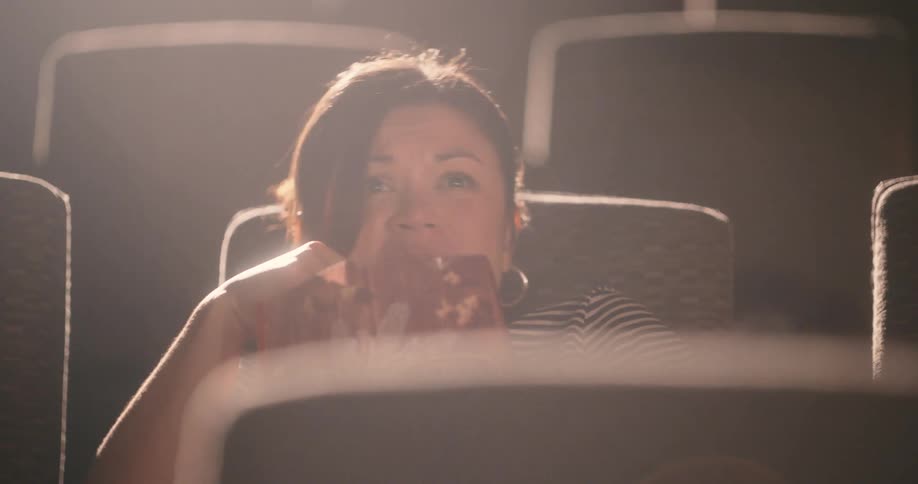 Woman sitting in a movie theater watching and eating popcorn