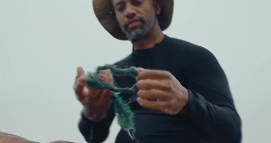 Man floating in a kayak on the water and we pick up a dirty rope from the sea and put it inside a bag