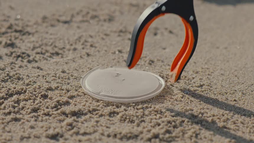 Plastic pincers picking up the lid from a plastic cup from the sand on a beach