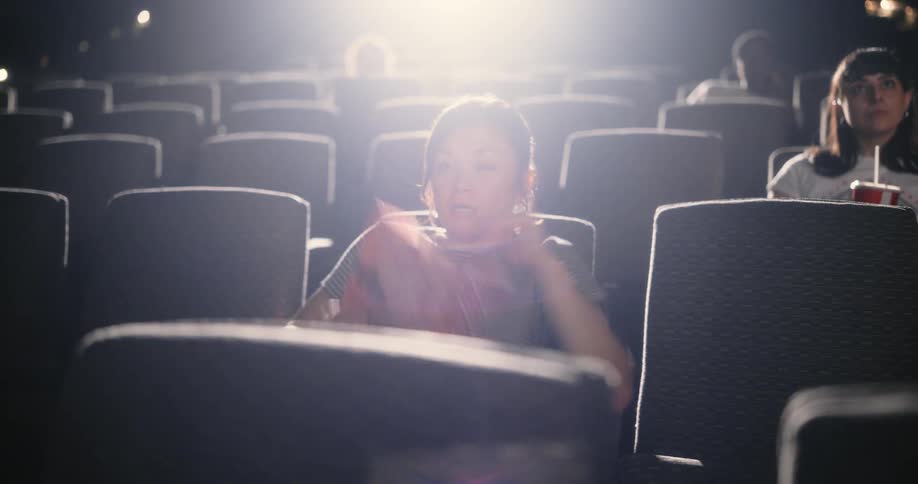 A woman watching a movie in a theater gets scared and spills her popcorn