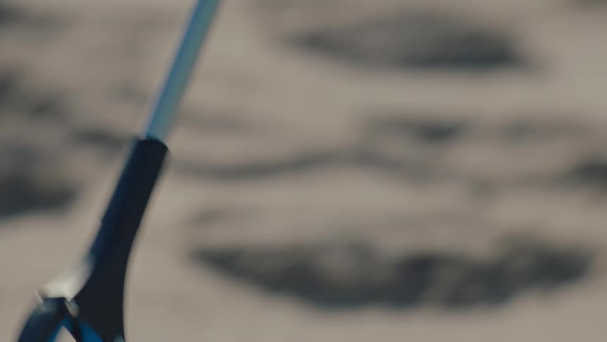 Person handling a tool that collects trash from the sand on the beach