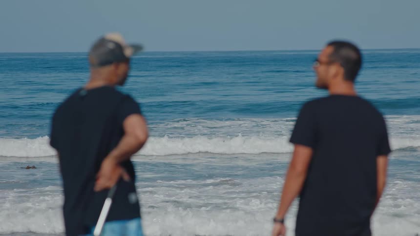 Two friends talking to each other standing in front of the ocean as waves roll in