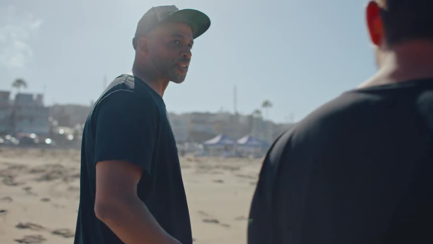 Two male friends are walking along the beach talking and laughing
