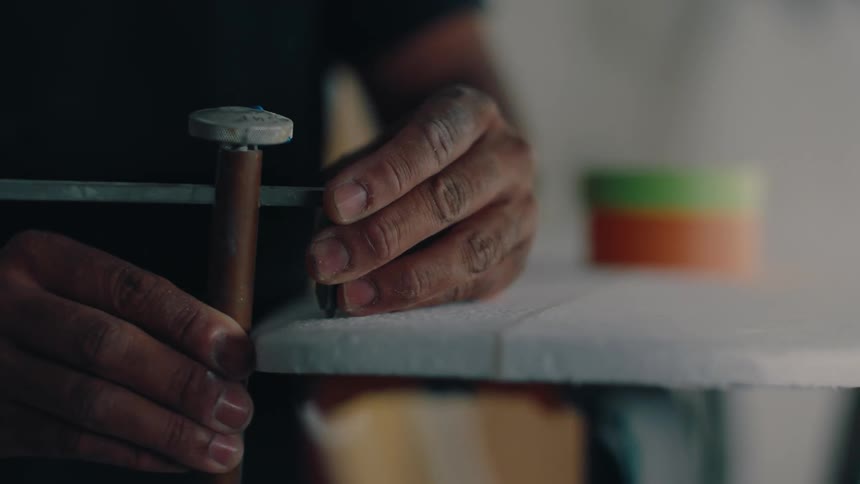 Close up of a person using a tool to trim the edge of a surfboard