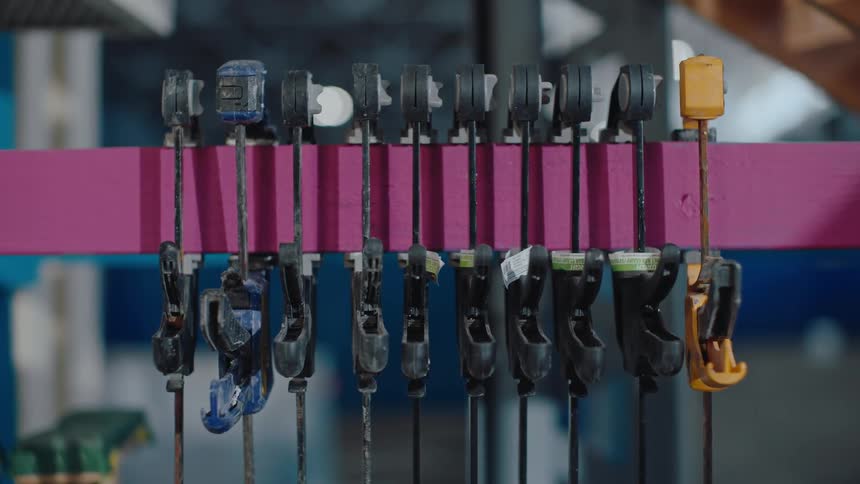 Various clamps hang on a piece of pink wood inside a building