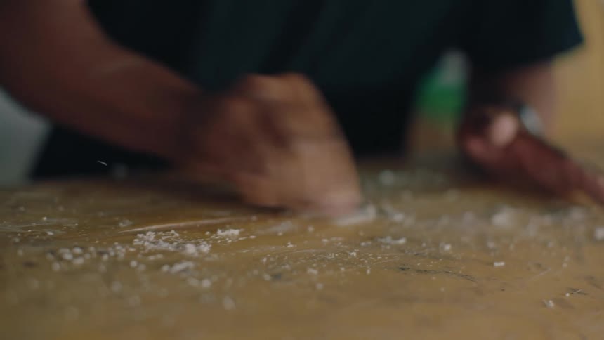 A mans hand scraping an object on a surface and several white flakes come out