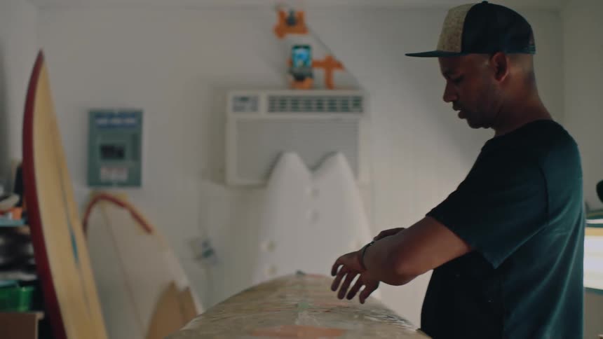 Man in a room with a surfboard adjusting his wristwatch