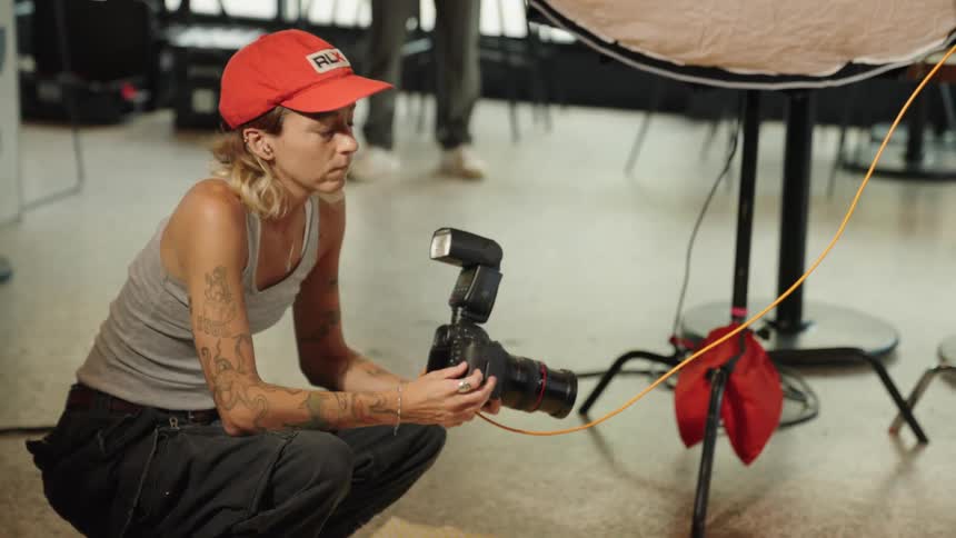 A photographer crouching on the floor holding a professional camera with a flash inserting a memory card