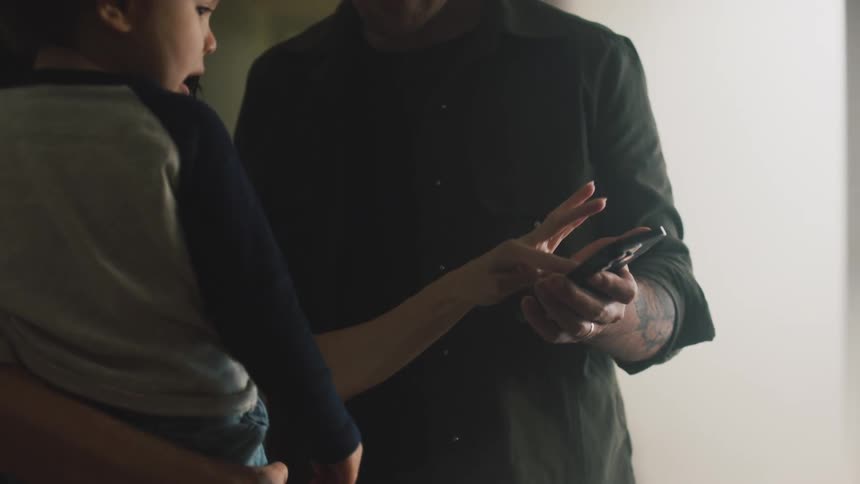 A man holding a cell phone and a woman holding a little girl is touching it with her finger