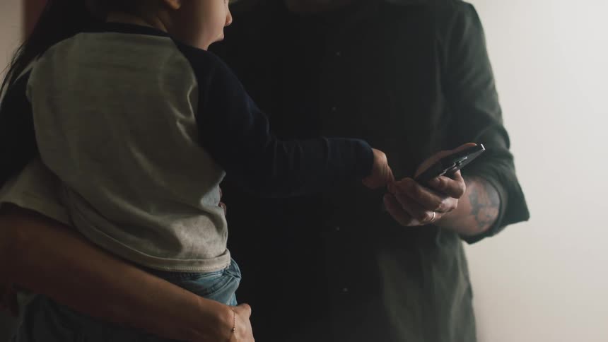 Mother with her small child on her lap next to the father who is holding a smartphone and the child touches the screen