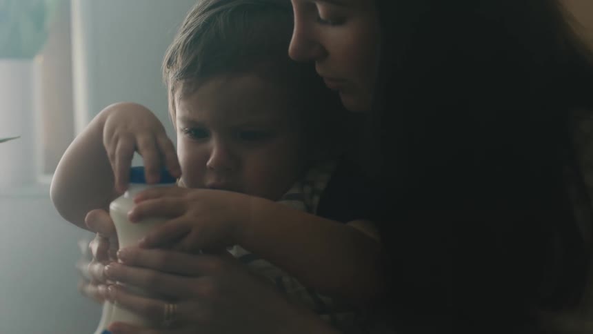 Mother holds her son while she helps him take the lid off a jar