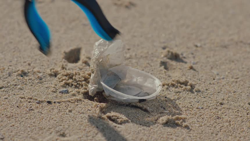 Accessory collecting plastic cup thrown on the beach sand