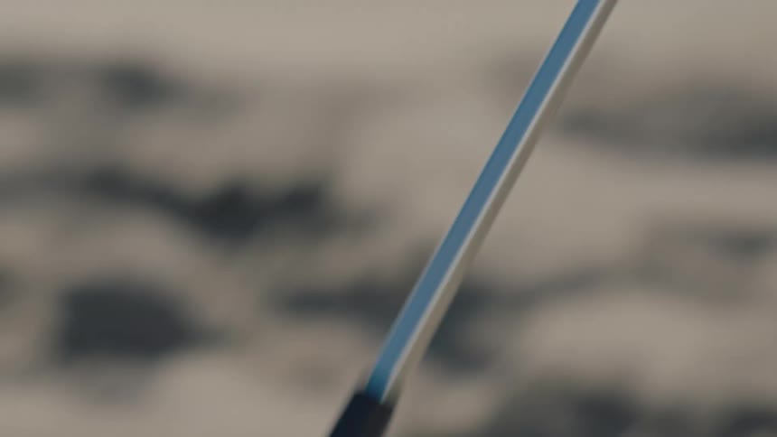 A closeup of a gripping tool collecting plastic debris from a sandy beach
