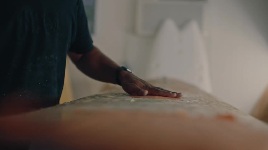 A man who works on surfboards rubs a board and then sets down a roll of tape