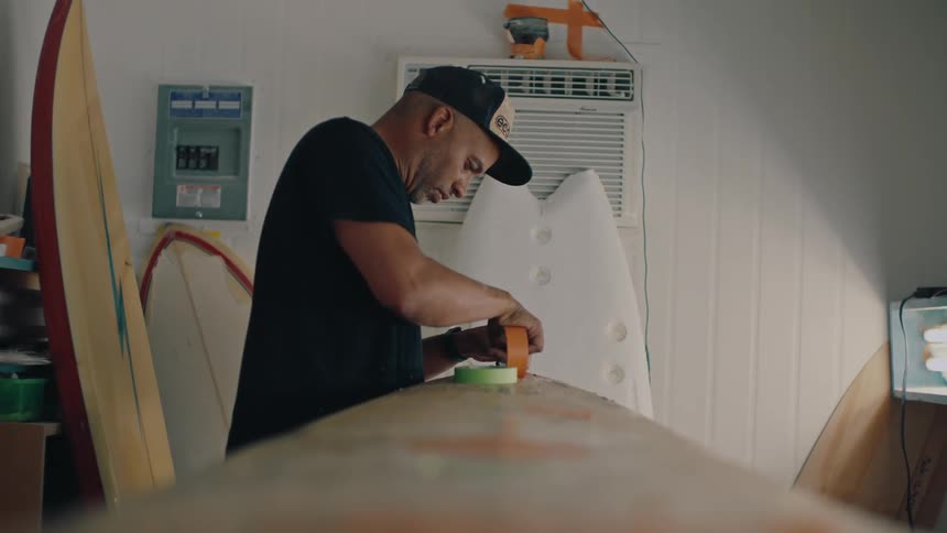 Man indoors sticking tape to a surfboard