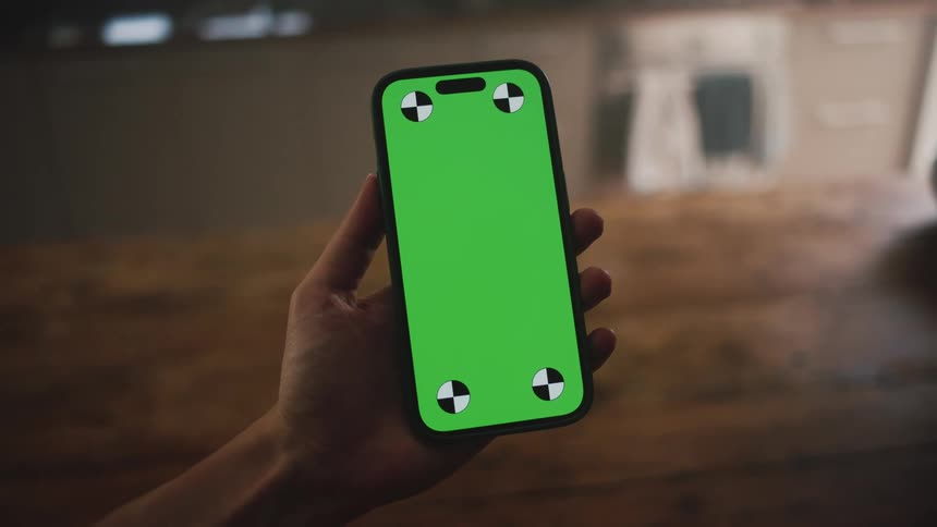 A hand holding a smart phone with a replaceable green screen
