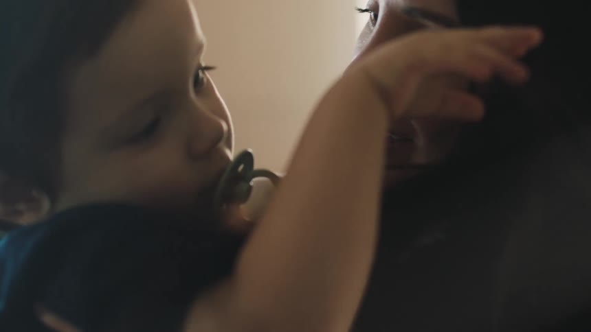 A little baby boy using a pacifier playing with his mothers hair and she is smiling
