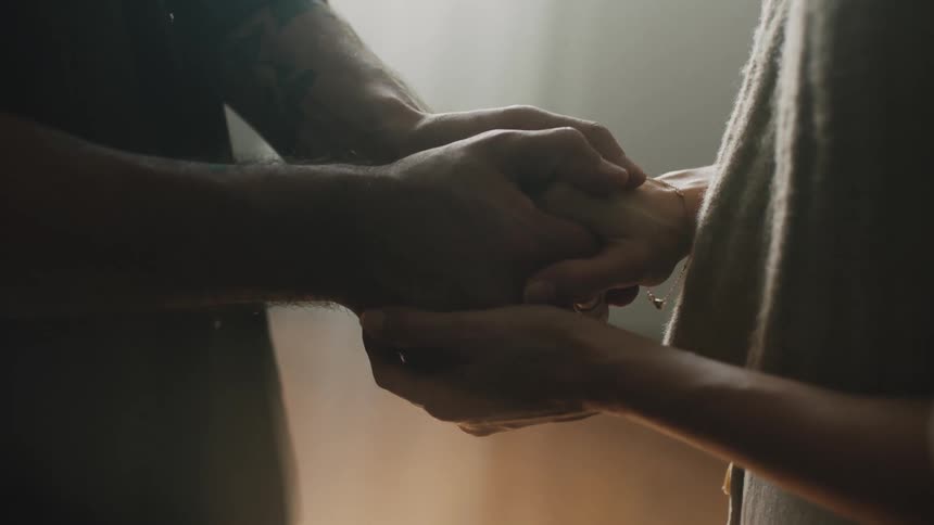 A romantic couple stands facing each other and holds hands between them