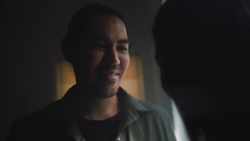 Man smiles while interacting with a laughing woman in a dimly lit room