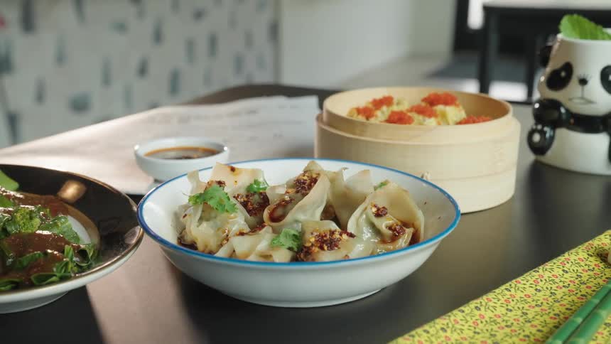 A bowl contains dumplings garnished with herbs next to a bowl of rice topped with orange roe