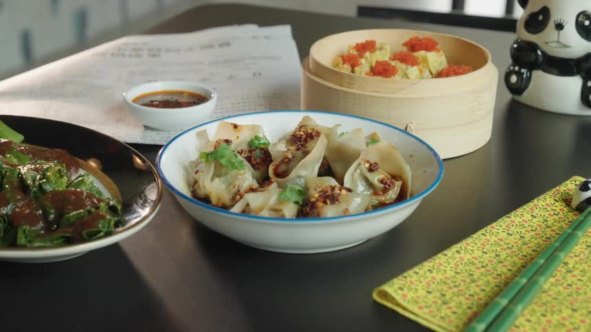 A dining table with dumplings in a blue bowl and a bamboo steamer with dim sum topped with roe